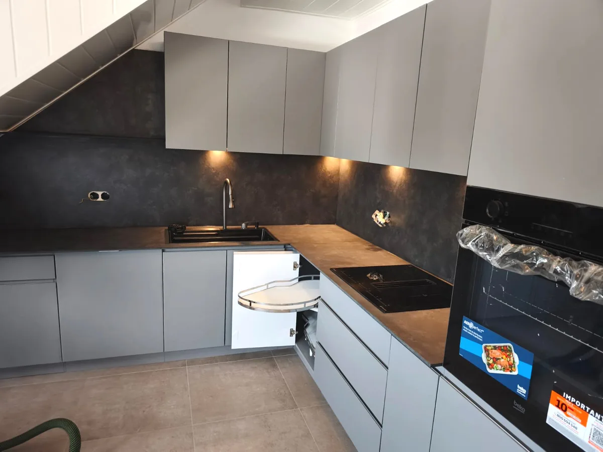 Graue Dachgeschossküche mit geöffnetem Eckschrank, ausschwenkbaren Böden und dunkler Rückwand