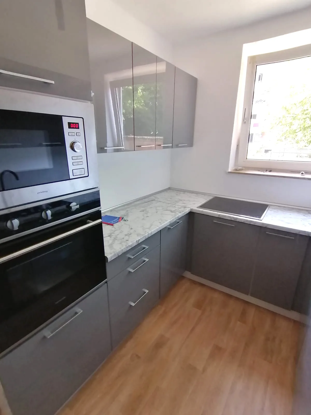 Kleine graue Hochglanzküche mit Arbeitsplatte in Marmoroptik und Mikrowelle über dem Backofen