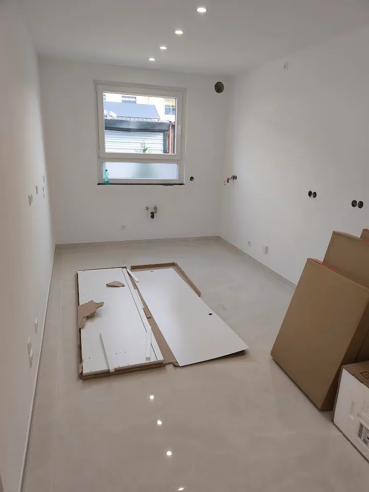 Empty room before installation, with connections and space for the sink by the window