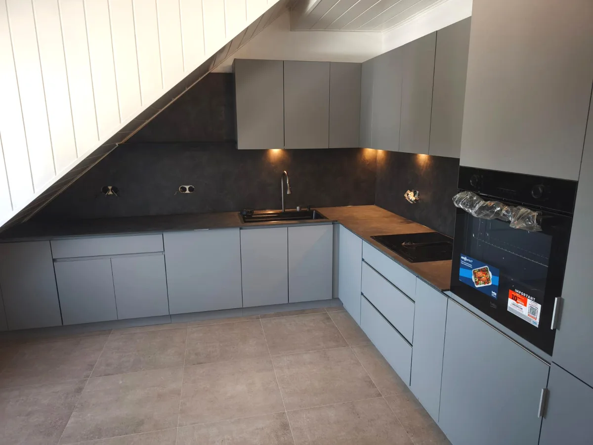 Grifflose Küche in mattem Grau unter der Dachschräge, mit dunkler Rückwand in Steinoptik