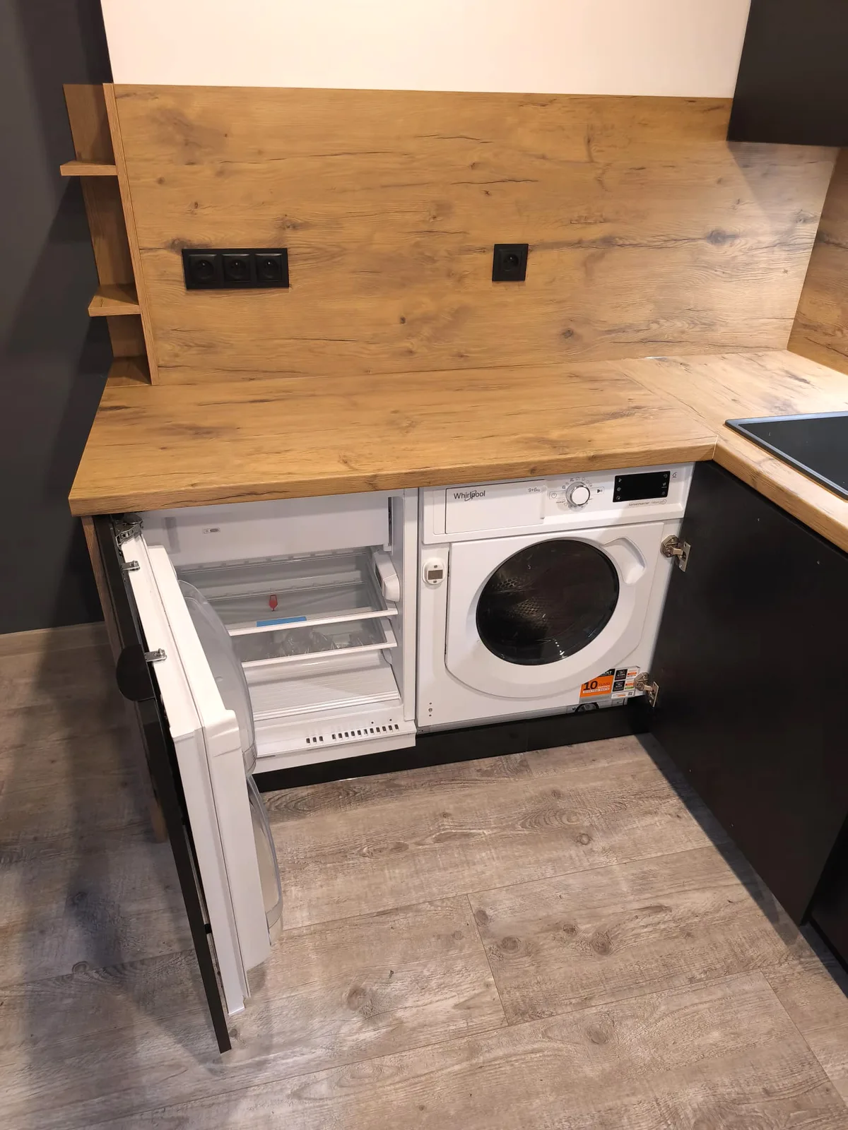 Unterbaukühlschrank und Einbauwaschmaschine hinter schwarzen Fronten unter einer Arbeitsplatte in Eiche-Optik