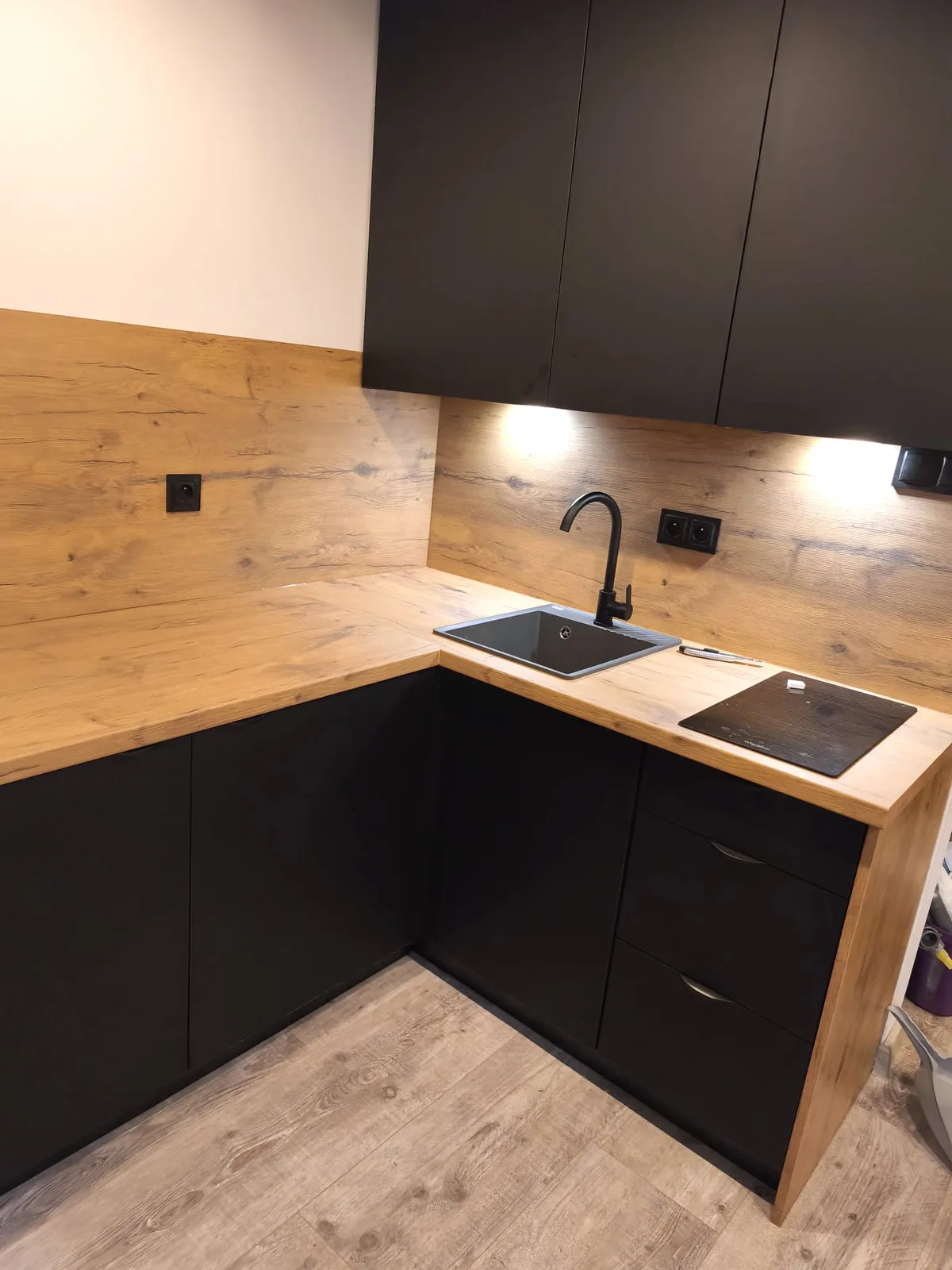 Mattschwarze L-Küche mit schwarzer Spüle, Arbeitsplatte und Wandpaneel in Eiche-Optik